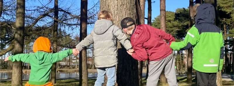 Tre barn holder hender og leker i det grønne landskapet, et symbol på samhold, trygghet og fellesskap. Foto.